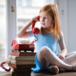 pensive little girl talking on vintage phone while sitting on table in light living room